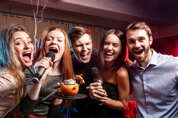 young caucasian students gathered to sing in karaoke bar, having fun together, karaoke and smoking...
