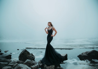 Sexy Woman long black dress silhouette mermaid tail fish. background river ice water stones cold...