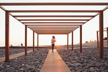 Charming girl supporter of a healthy lifestyle runs along the sunny morning beach along a wooden walkway. The concept of a beautiful body and a healthy lifestyle