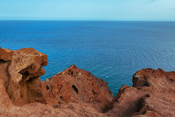 A view of the sea behind the orange rocks on on a beach in Tenerife in the coastline of a tropical island. With orange and blue. With copy space.