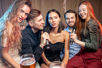 group of young caucasian people in party clothes have free time. leisure time in karaoke bar, enjoy singing, drinking