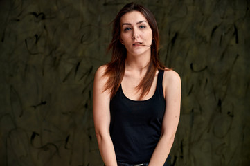 Beauty concept, stylish portrait. Photo of a pretty glamorous brunette girl in a black t-shirt with flying hair on a gray fashionable original background.