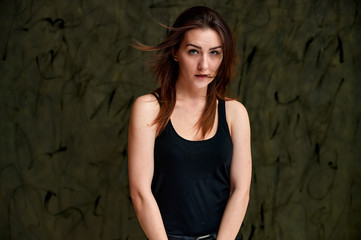 Fototapeta premium Beauty concept, stylish portrait. Photo of a pretty glamorous brunette girl in a black t-shirt with flying hair on a gray fashionable original background.
