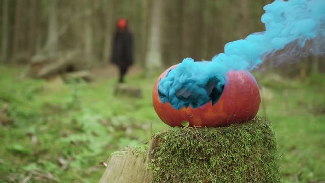 Person goes in mask and coak in the forest on the halloween with smoky pumpkin