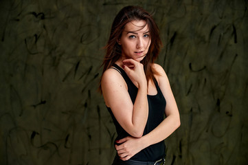 Fototapeta premium Beauty concept, stylish portrait. Photo of a pretty glamorous brunette girl in a black t-shirt with flying hair on a gray fashionable original background.