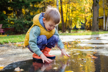 toddler boy sitting in puddle in rubber rain boots