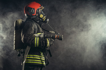 young firefighter in uniform stand in smoky background wearing uniform, safety concept