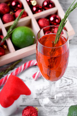 Red alcoholic drink in a tall glass surrounded by Christmas attributes against white wooden background