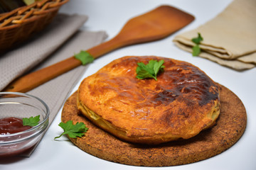 An Australian meat pie on a white background. Wooden spatula in the back.