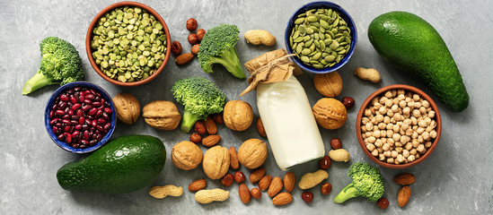 Vegan protein source,banner. Healthy diet food: milk, legumes, pumpkin seeds,peas, nuts,avocado and broccoli on a gray concrete background. Top view, flat lay, border.