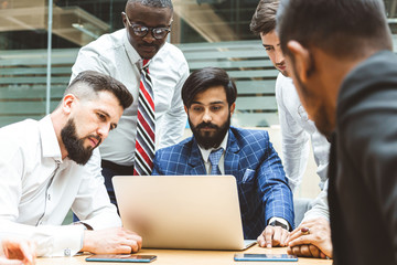 A team of young office workers, businessmen with laptop working at the table, communicating together in an office. Corporate businessteam and manager in a meeting. coworking.