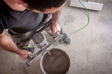 Bauarbeiter rührt Ausgleichsmasse an, spachtelt den Fußboden und bereitet so den Boden für das Parkettlegen vor - obrazy, fototapety, plakaty
