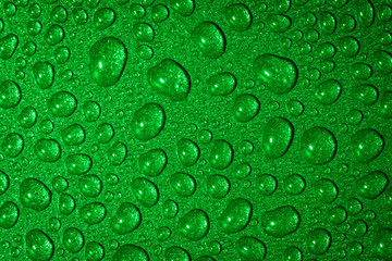 A close up abstract macro photo of water droplets on a grey non stick frying pan material lit with a green flash gel