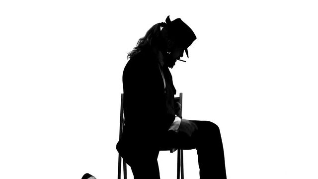 Silhouette Elegant man in a black hat is dancing an erotic dance. He uses a chair and a cigarette. White background. Close up, slow motion.