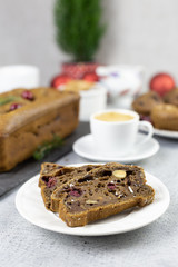 a piece of chocolate cake with nuts, berries and chocolate drops on a white plate and a whole cake in the background