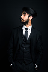Portrait of a young handsome successful Indian in a classic black three-piece business suit on a dark background