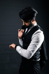 Portrait of a young handsome successful Indian in a classic black three-piece business suit on a dark background, Holding his jacket over his shoulder