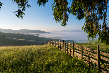 Obraz premium Mountain meadow in a sunrise enclosed by a wooden fence