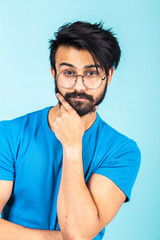 Emotional portrait of a handsome Hindu man in a blue T-shirt on a bright blue background, think about something