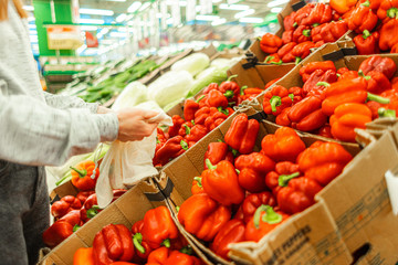 Shopping at the supermarket. The girl in the store chooses peppers in the vegetable department. A healthy and balanced diet.