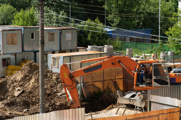 Work excavator at a construction site. An orange large excavator digs a ditch in dirty soil. A worker looks out the window and does.