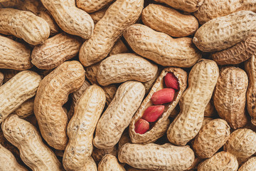 Peanut cores in a shattered pod among unpeeled peanuts. Food background and texture. Top view, flat lay, copy space