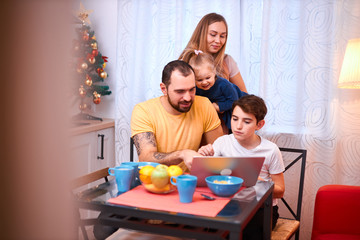 happy, cute, lovely caucasian family have breakfast together at home, dressed in casual wear, watching video on modern laptop at morning, adorable little daughter and son with young parents, enjoy