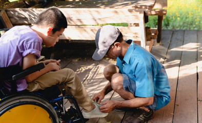 Father tying a shoe to his son on wooden house with nature light,The boy is Disabled child,Special children's lifestyle,Life in the education age of special need children,Happy disability kid concept.