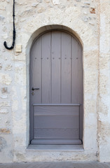 Old Grey door in an arched stone doorway with wooden panelling.
