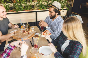 A company of multicultural  young people in a cafe eating pizza, drinking cocktails, having fun