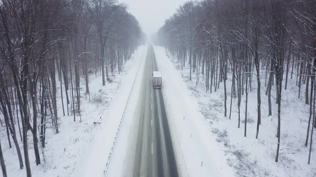 Aerial view of truck driving on a road surrounded by winter forest in snowfall