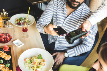 Young attractive Hindu man paying in cafe with contactless smartphone payment