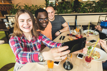 Group of young cheerful friends are sitting in a cafe, eating, drinking drinks. Friends take selfies and take pictures.