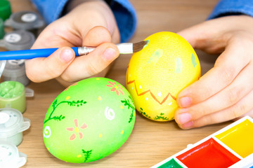 Close-up hands of a boy holding a brush for painting eggs for Easter. Preparation for the holiday, the child paints flowers on the egg, his fingers are dirty.