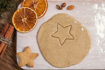 Christmas homemade baking background: ginger dough rolled out on a wooden board, cookies, cinnamon and slices of dried oranges. Top view, flat lay, copy space.