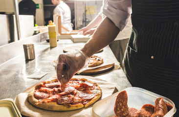 Professional chef cooking in the kitchen restaurant at the hotel, preparing dinner. A cook in an apron makes a salad of vegetables and pizza.