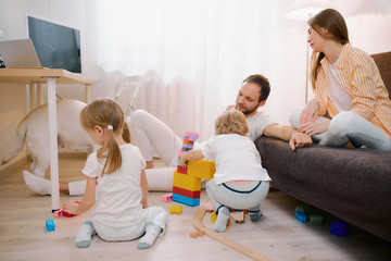 Obraz na płótnie Canvas caucasian children, son and daughter playing on floor together while their parents relax or busy with their own affairs at home, happy family concept