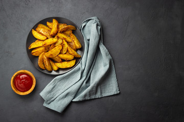 Baked potato with spices and ketchup in a black plate. Dark background. Top view with copy space.