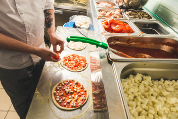Professional chef cooking in the kitchen restaurant at the hotel, preparing dinner. A cook in an apron makes a salad of vegetables and pizza.