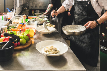 Professional chef cooking in the kitchen restaurant at the hotel, preparing dinner. A cook in an apron makes a salad of vegetables and pizza.