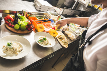 Professional chef cooking in the kitchen restaurant at the hotel, preparing dinner. A cook in an apron makes a salad of vegetables and pizza.