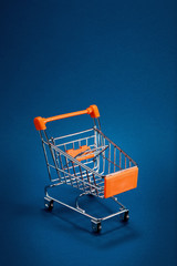 Empty shopping cart trolley on blue background with copy space