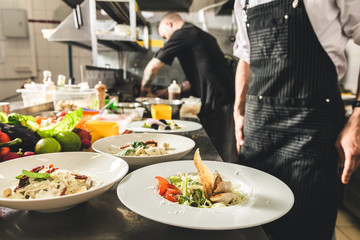 Professional chef cooking in the kitchen restaurant at the hotel, preparing dinner. A cook in an apron makes a salad of vegetables and pizza.