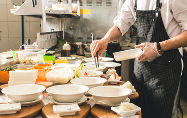 Professional chef cooking in the kitchen restaurant at the hotel, preparing dinner. A cook in an apron makes a salad of vegetables and pizza.