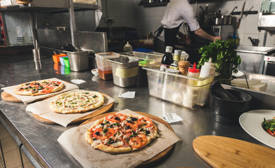Professional chef cooking in the kitchen restaurant at the hotel, preparing dinner. A cook in an apron makes a salad of vegetables and pizza.
