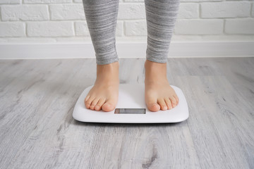 Woman legs staying on weighing scales, white brick wall background. Healthcare, diet concept. Close-up, copy space