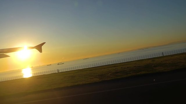 Airliner taking off at Tokyo Haneda International Airport in sunrise time. Big bright sun light up the sea, golden reflection on surface. Near the Keihin industry region. Tokyo, Japan. 4K UHD