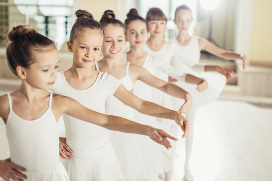 Young happy caucasian little ballerinas, awesome ballet dancers practicing some dance element in a dance class. Professional school of ballet dance for kids, chiildren