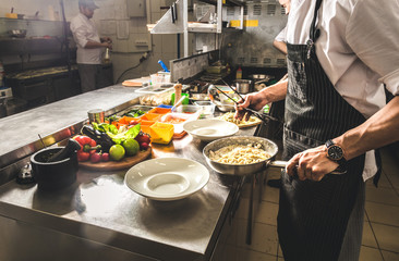 Professional chef cooking in the kitchen restaurant at the hotel, preparing dinner. A cook in an...