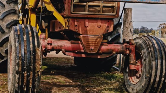 An old and rusty tractor reverses into the paddocks of a farm in slow motion